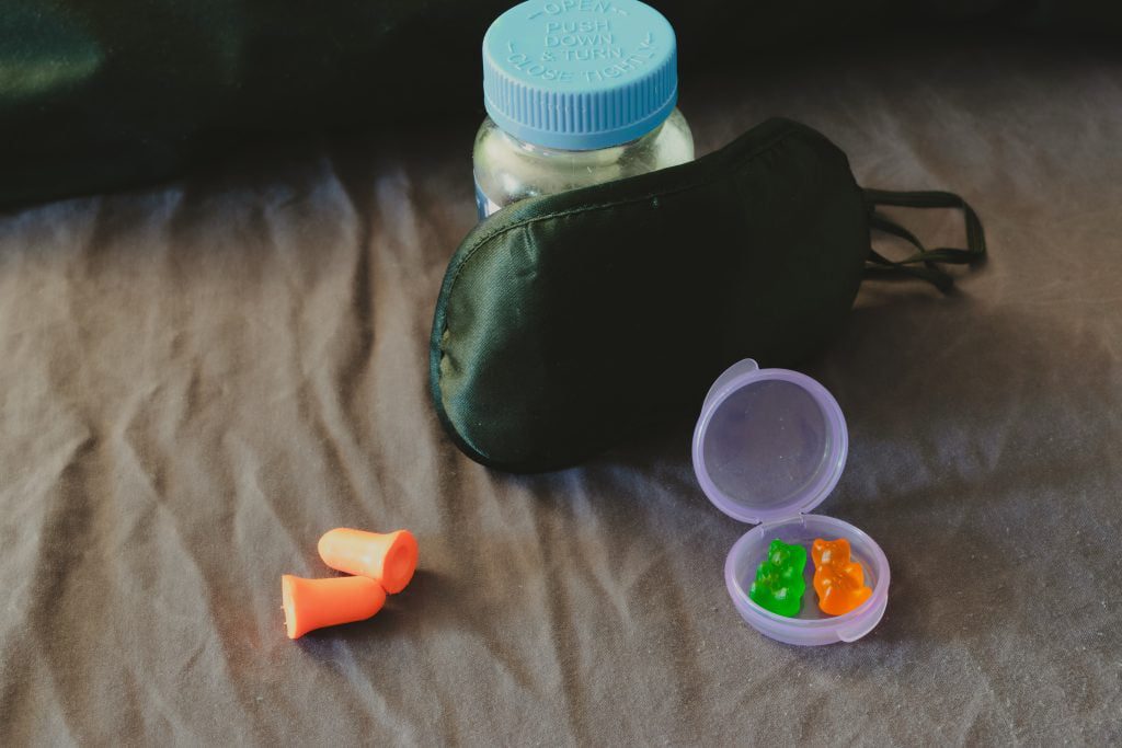 Bear shaped sleep gummies in front of an eye mask leaning on a bottle and ear plugs to the left.- sold on stock photo sites