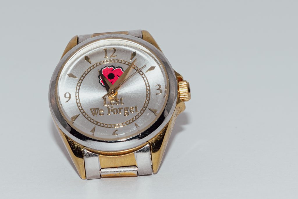 A gold and silver watch set to eleven minutes after eleven o'clock. It says Lest We Forget and has a red poppy on it. - sold on stock photo sites